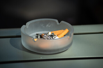 Used glass ashtray filled with cigarette butts and ash on an outdoor surface. Reflects smoking habits.