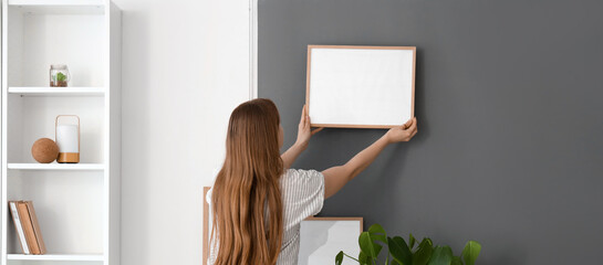 Young woman hanging frame on wall at home
