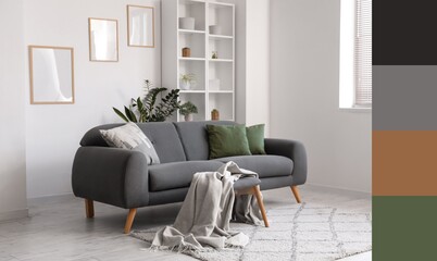Grey sofa with cushions and plaid, shelving unit and frames on white wall in living room. Different color patterns