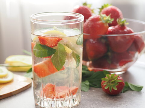 woman making refreshing homemade lemonade detox drink or cocktail summer with ice. Refreshing vibrant summer drinks with lemon, strawberry and mint and colorful straws on the table