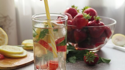 woman making refreshing homemade lemonade detox drink or cocktail summer with ice. Refreshing vibrant summer drinks with lemon, strawberry and mint and colorful straws on the table