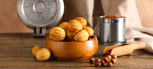 Bowl with tasty walnut shaped cookies, boiled condensed milk and hazelnuts on wooden table