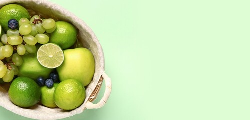 Basket full of different fresh fruits on green background with space for text, closeup