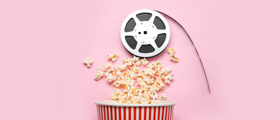 Bucket with tasty popcorn and film reel on pink background