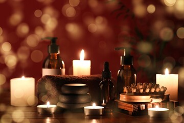 Massage body brush, spa stones, bottles of cosmetic products and burning candles on table