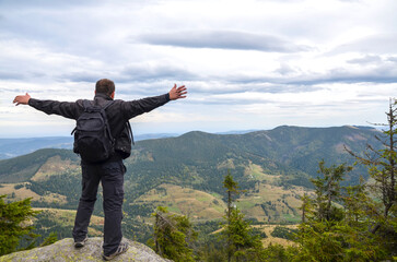 Man with arms outstretched standing on a mountain peak, overlooking an expansive vista of green...