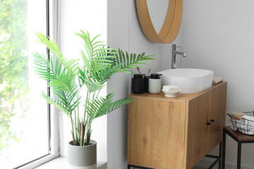 Sink bowl and bath accessories on wooden cabinet in interior of light bathroom