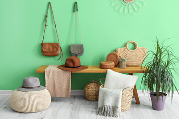 Wooden bench with wicker baskets, hats and purses near green wall