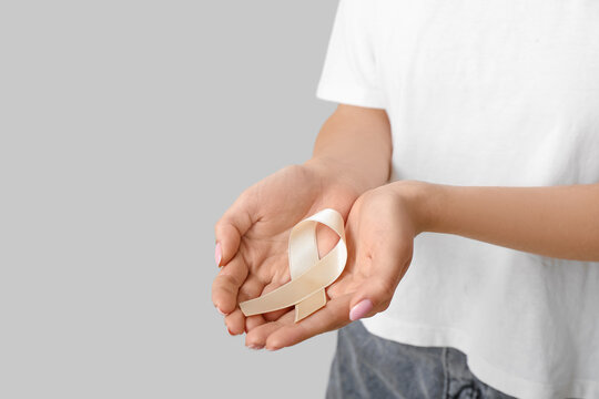 Woman with beige ribbon on light background, closeup. Uterine cancer awareness concept