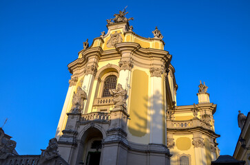 Ornate Baroque facade of St. George's Cathedral with yellow walls and statues stands against a clear blue sky in Lviv, Ukraine
