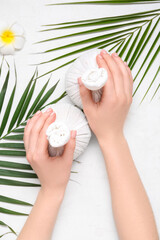 Female hands with herbal massage bags and palm leaves on light background, closeup