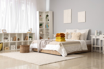 Stack of warm knitted sweaters on bed in modern bedroom