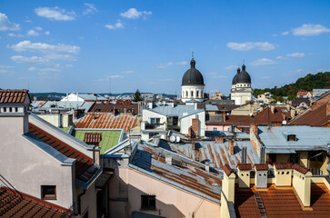 Panoramic view of Lviv's rooftops with diverse textures and colors, dominated by prominent Transfiguration church domes against a clear blue sky