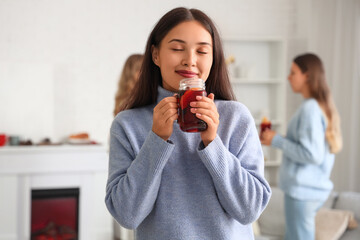 Pretty young woman with glass of warm mulled wine in living room at party
