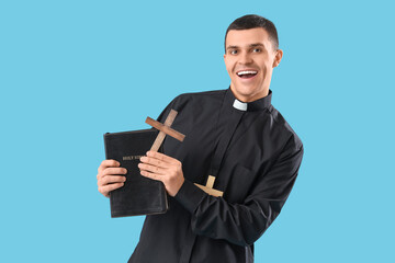 Young priest with Holy Bible and crosses on blue background