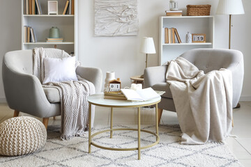 Interior of light living room with cozy armchairs and books on coffee table