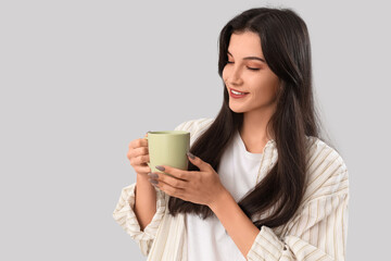 Pretty young woman with cup of tea on grey background