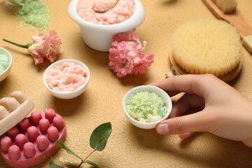 Female hand with different body scrubs and bath supplies on color background, closeup