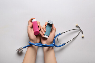 Child's hands with asthma inhalers and stethoscope on white background