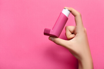 Child's hand with asthma inhaler on pink background