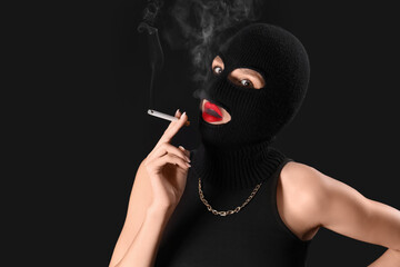 Beautiful young woman in balaclava smoking cigarette on black background