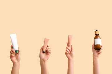 Female hands with bottle and tubes of different cosmetic products on beige background