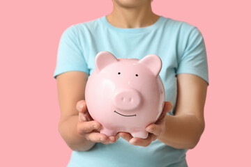 Mature woman with piggy bank on pink background