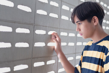 A teenage boy gently touches a patterned cement wall, staring through the light holes with a curious and introspective gaze.