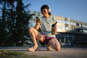 Mature japanese woman athlete hold shaker and cellphone after jogging