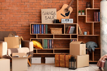 Many various unwanted things and cardboard with text GARAGE SALE near brick wall in room