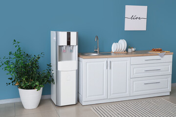 Interior of stylish kitchen with modern water cooler near blue wall