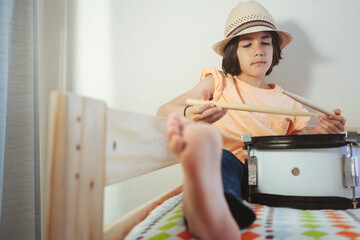 Boy practicing with drumsticks on bed in peaceful setting