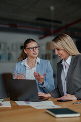Businesswomen collaborating on laptop, analyzing data and discussing strategies in modern office