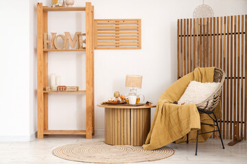 Coffee table with lamp, teapot, cup of tea and armchair in interior of living room