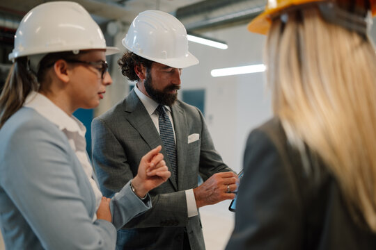 Engineers and businessman discussing project on tablet in factory