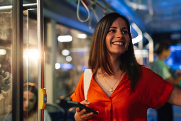 Smiling woman using smartphone on public transport at night