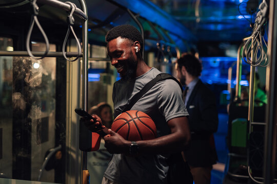 Smiling basketball player using smartphone on public transport at night