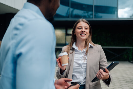 Businesswoman holding coffee and tablet talking with businessman outdoors