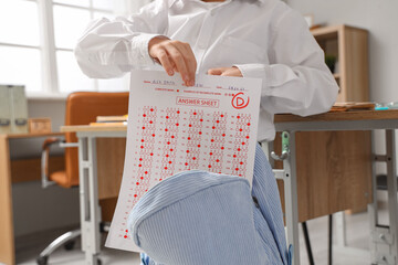 Schoolboy putting answer sheet form into backpack in classroom, closeup