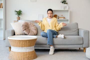 Shocked young woman sitting on sofa at home