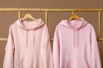 Stylish hoodies hanging on ladder against brown background