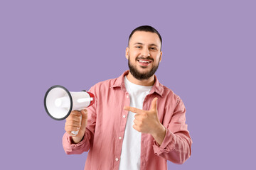 Handsome young man pointing at megaphone on lilac background