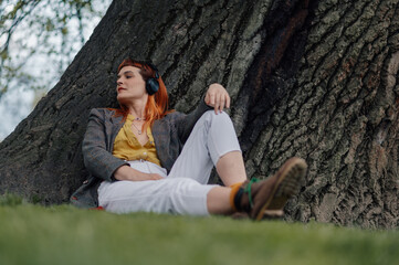 Creative woman relaxing under tree listening music with headphones