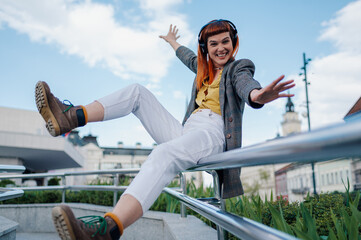 Carefree stylish woman listening music with headphones and dancing in city center