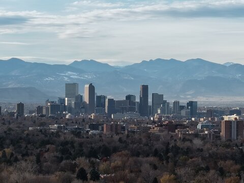 Iconic Denver skyline framed by the majestic, hazy Rocky Mountains under a cloudy sky. This vibrant city view captures the modern skyscrapers of downtown against the stunning nature