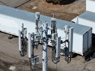 Close-up aerial drone shot of a modern cell tower bristling with 5G antennas and telecommunications equipment, symbolizing advanced connectivity. 