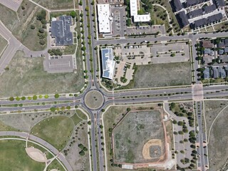 Dynamic aerial view of a suburban hub featuring a prominent roundabout, surrounded by mixed-use...