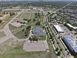 Expansive aerial view showcasing a diverse urban landscape in Colorado, featuring educational facilities with sports fields, modern commercial buildings with solar panels, and suburban residential 
