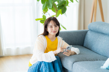 部屋でスマホを操作する若い女性