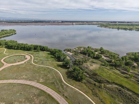 Aerial view of Cherry Creek Reservoir in Centennial, Colorado, showcasing tranquil waters reflecting the sky, surrounded by lush green parks and winding pathways. Ideal for themes of recreation